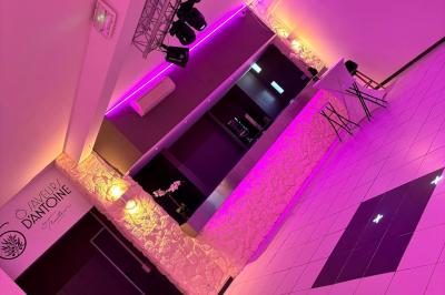 Salle de réception décorée avec des tables rondes, nappes blanches, chaises élégantes et éclairage violet tamisé.