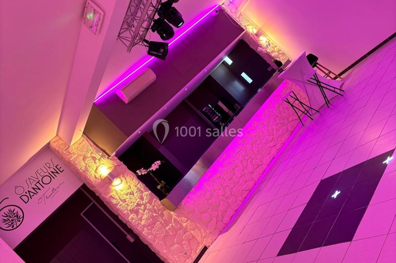 Salle moderne avec éclairage rose, comptoir en pierre, tables hautes et logo mural sur fond clair.