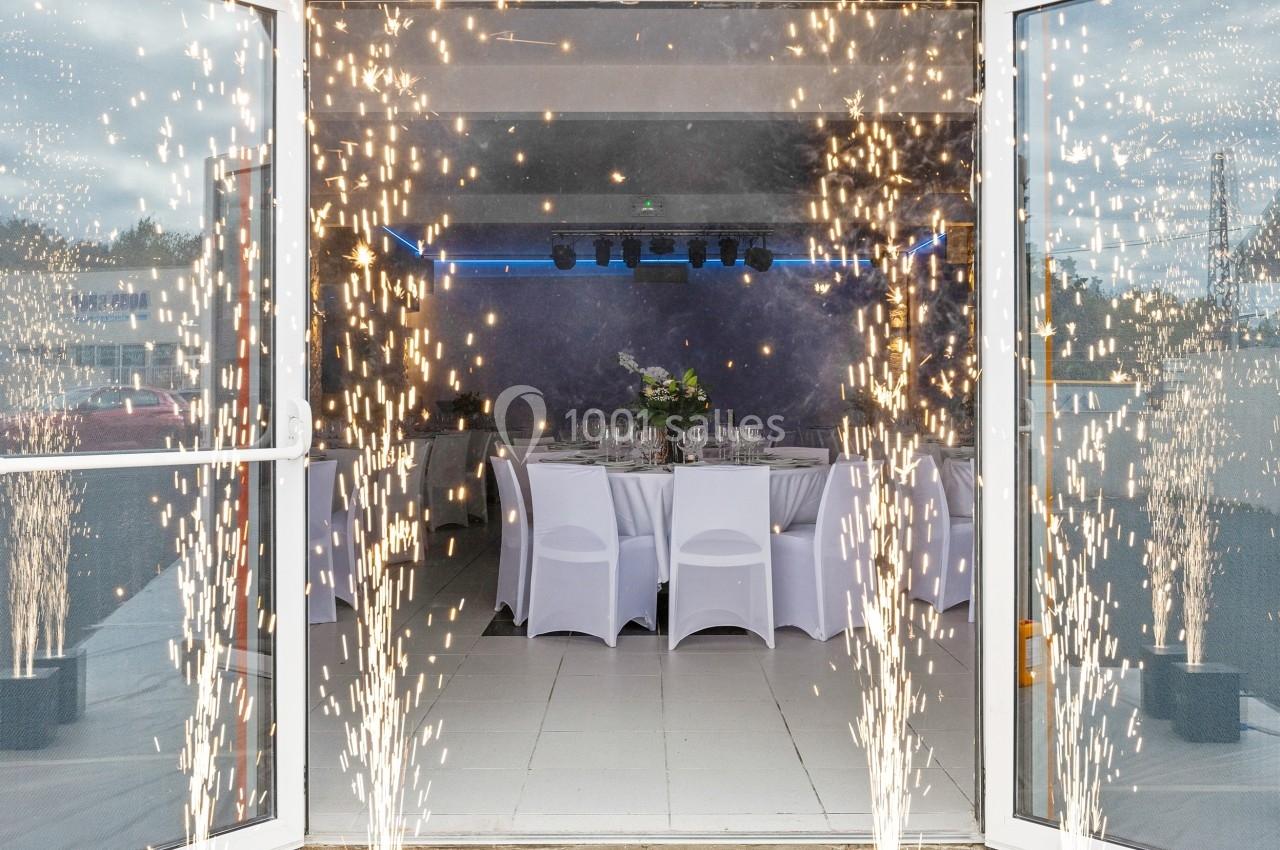 Salle de réception décorée avec des tables dressées, vue à travers des portes ouvertes entourées d'étincelles festives.