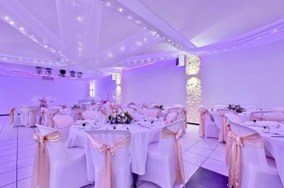 Salle de réception décorée avec des tables rondes, nappes blanches, chaises élégantes et éclairage violet tamisé.