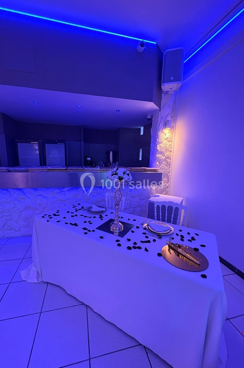 Table décorée avec une nappe blanche, pétales noirs et centre de table floral, dans une salle éclairée par des lumières…