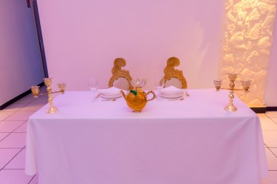 Salle de réception décorée avec des tables rondes, nappes blanches, chaises élégantes et éclairage violet tamisé.