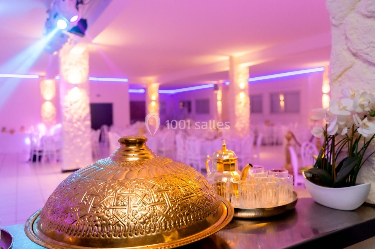 Salle de réception éclairée en rose avec un plateau doré, une théière et des verres au premier plan.