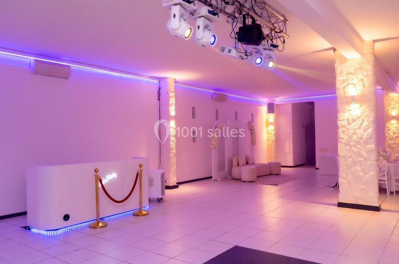Salle lumineuse avec éclairage LED violet, comptoir blanc, colonnes en pierre et mobilier minimaliste.