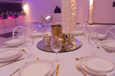 Salle de réception décorée avec des tables rondes, nappes blanches, chaises élégantes et éclairage violet tamisé.