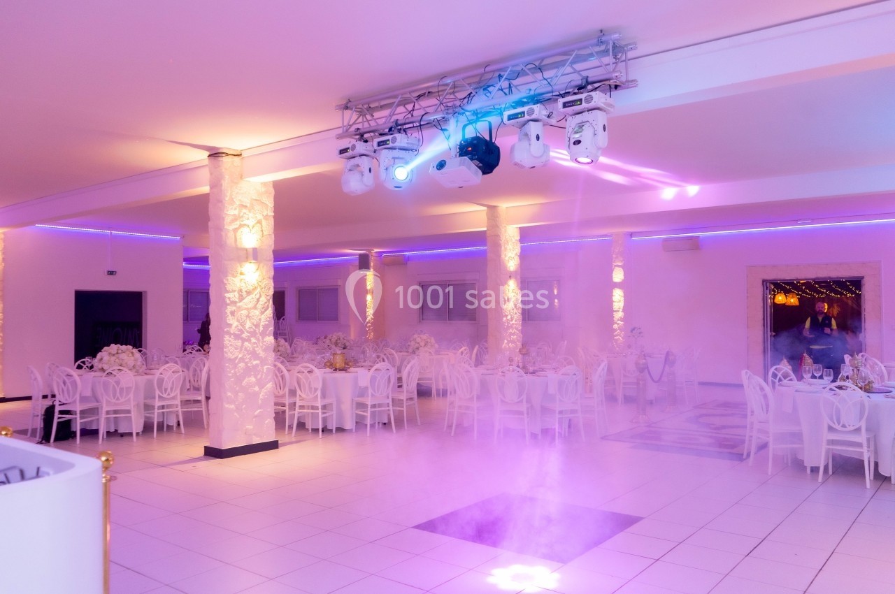 Salle de réception lumineuse avec tables rondes dressées, éclairage violet et projecteurs suspendus.