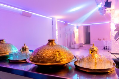 Salle de réception décorée avec des tables rondes, nappes blanches, chaises élégantes et éclairage violet tamisé.