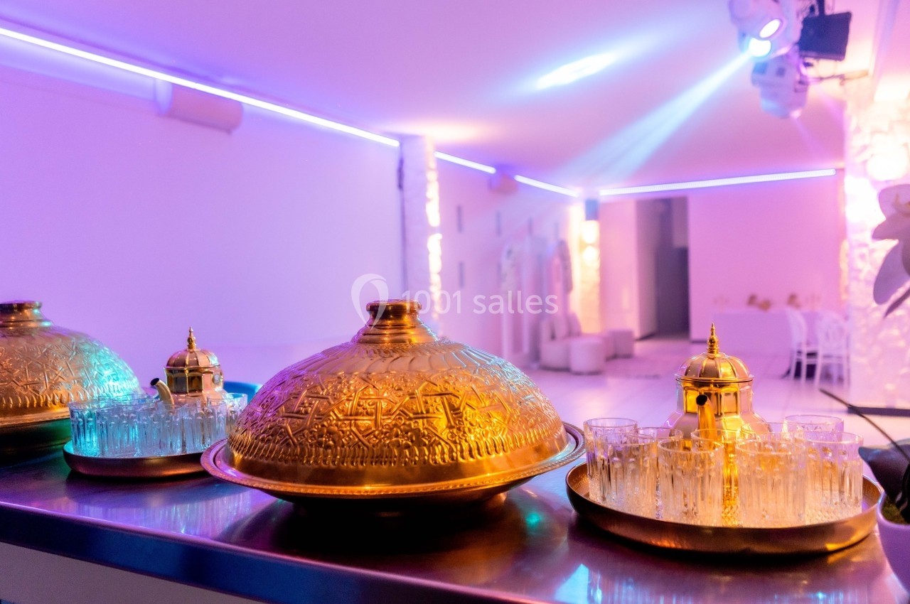 Plateaux dorés gravés avec des théières et des verres en verre, disposés sur une table dans une salle éclairée de lumières…