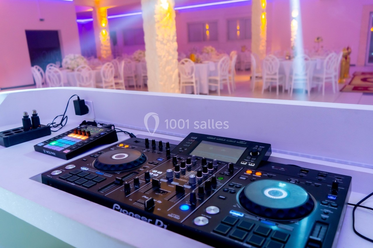 Console de mixage DJ avec platines et contrôleurs dans une salle de réception éclairée par des lumières colorées.