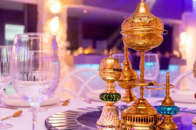 Salle de réception décorée avec des tables rondes, nappes blanches, chaises élégantes et éclairage violet tamisé.