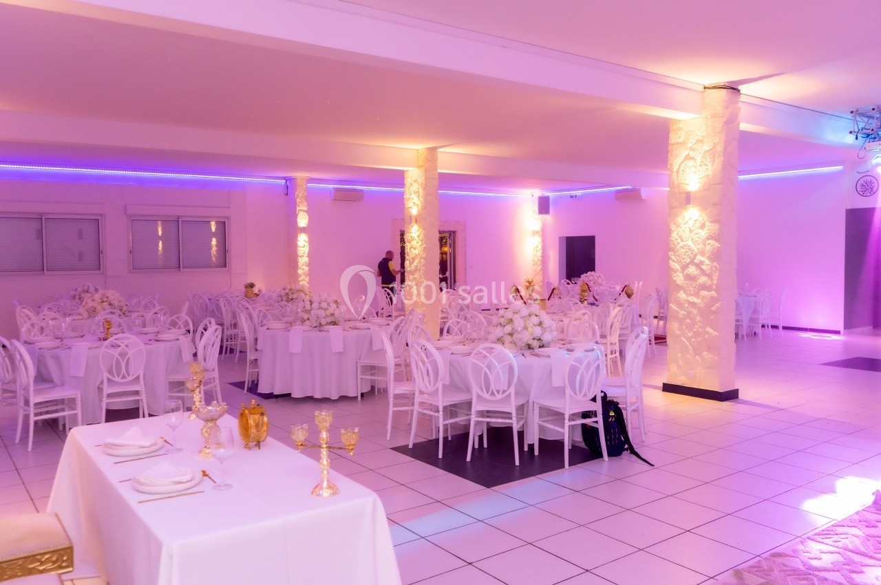 Salle de réception lumineuse avec tables décorées de nappes blanches, chaises assorties et éclairage violet.