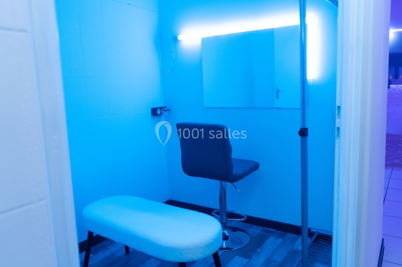 Salle éclairée en bleu avec un tabouret, un banc, un miroir mural et un support vertical.