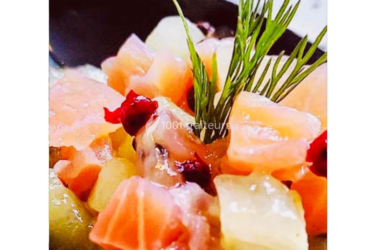 Dés de saumon, ananas et canneberges garnis d'aneth, présentés dans une assiette noire.