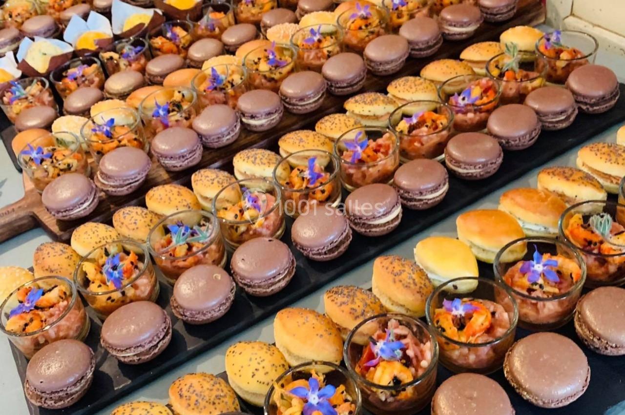 Plateaux garnis de macarons, verrines colorées et petits pains, décorés de fleurs comestibles.