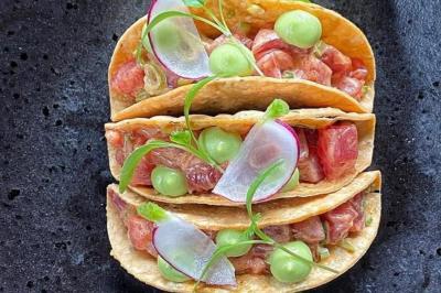 Dés de saumon, ananas et canneberges garnis d'aneth, présentés dans une assiette noire.