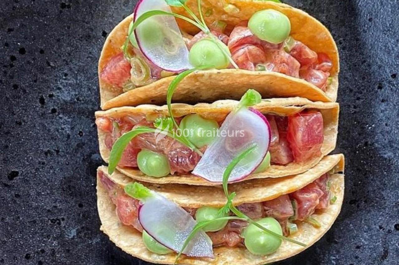 Tacos garnis de dés de poisson cru, tranches de radis, purée verte et herbes fraîches sur une assiette noire.