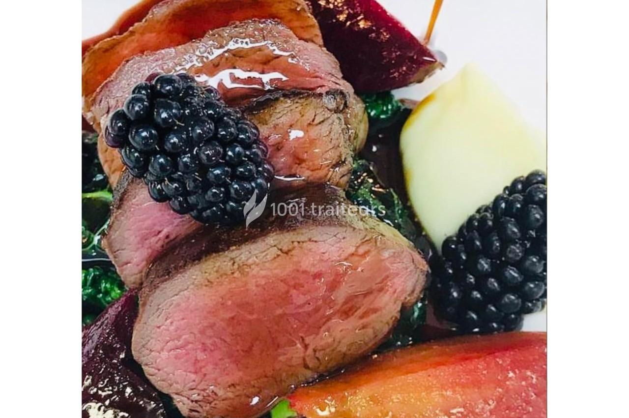 Assiette de viande rouge tranchée, accompagnée de mûres, purée et légumes colorés, nappée d'une sauce brillante.