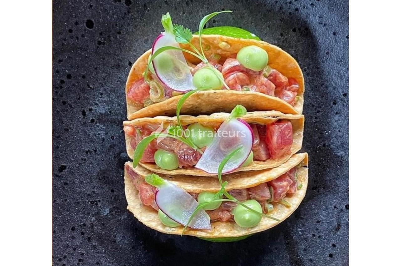 Trois tacos garnis de poisson cru, radis, purée verte et herbes fraîches, présentés sur une assiette noire.