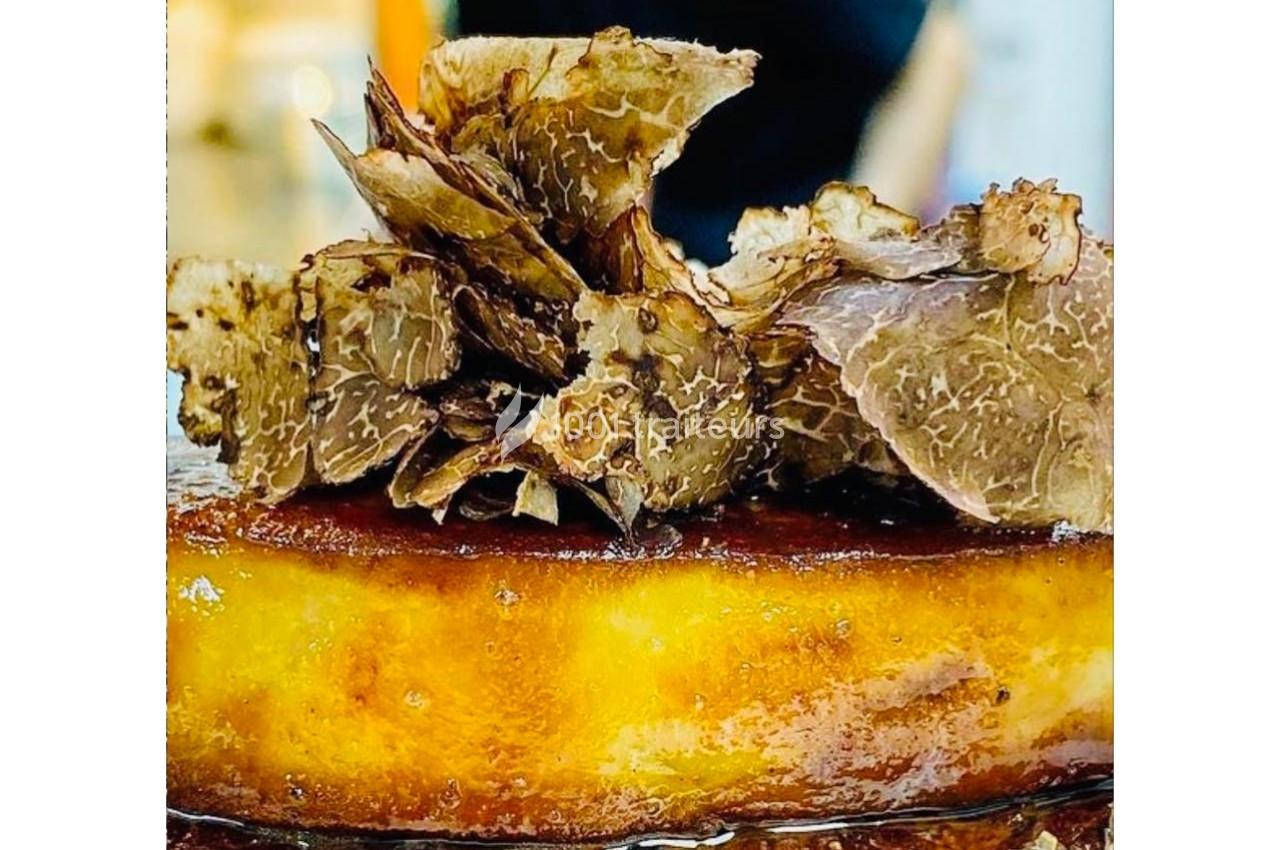 Gâteau doré garni de fines tranches de truffe noire, présenté dans un environnement lumineux.