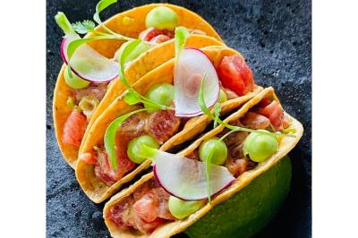 Dés de saumon, ananas et canneberges garnis d'aneth, présentés dans une assiette noire.