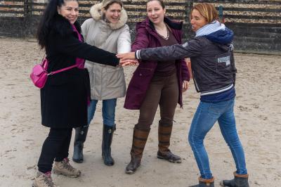 Femme souriante tenant les rênes d'un cheval brun dans un environnement extérieur boisé.