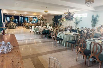 Salle de réception avec table dressée, chaises en bois sculpté, nappes vertes et décorations florales élégantes.