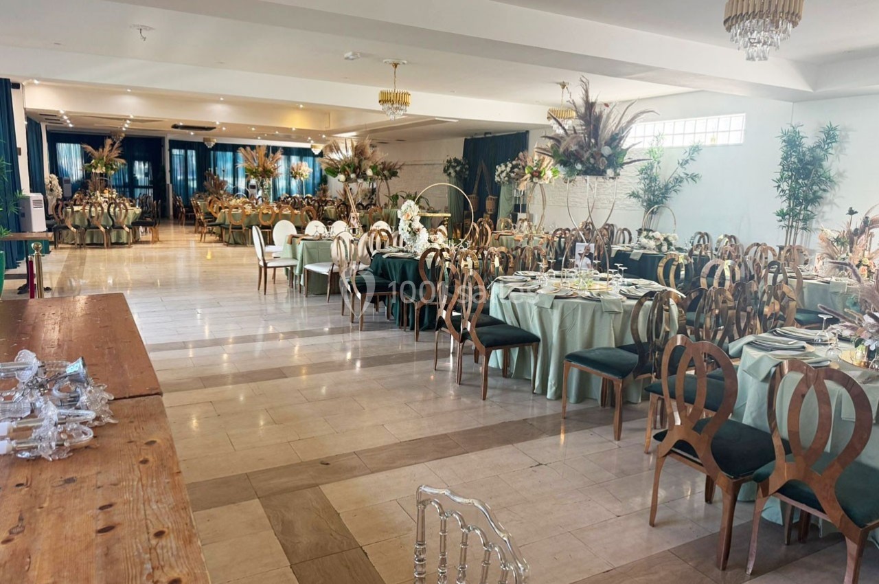 Salle de réception élégamment décorée avec des tables rondes dressées, des chaises en bois sculpté et des arrangements…