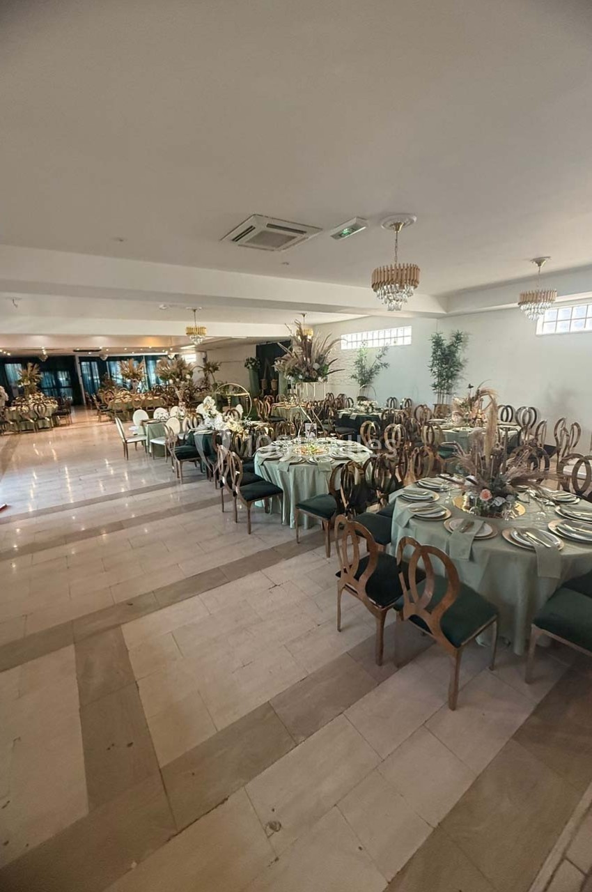 Salle de réception élégante avec tables dressées, nappes vertes, chaises en bois et décorations florales.