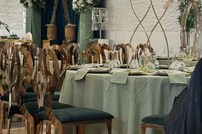Salle de réception avec table dressée, chaises en bois sculpté, nappes vertes et décorations florales élégantes.