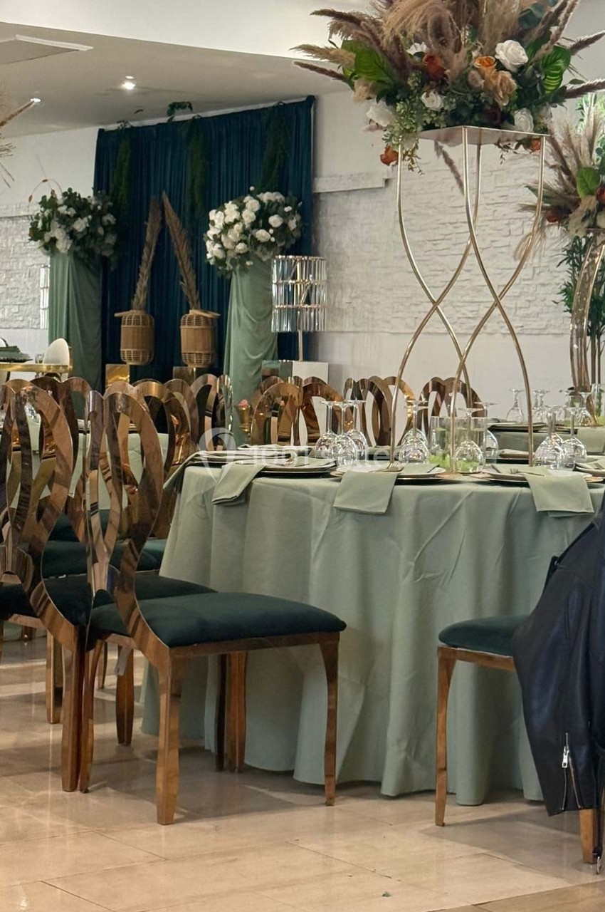 Salle de réception avec table dressée, chaises en bois sculpté, nappes vertes et décorations florales élégantes.