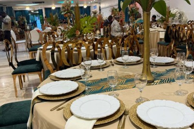Salle de réception avec table dressée, chaises en bois sculpté, nappes vertes et décorations florales élégantes.