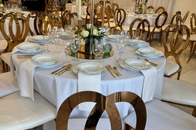 Allée centrale décorée de fleurs blanches menant à une arche florale, entourée de chaises blanches en extérieur.