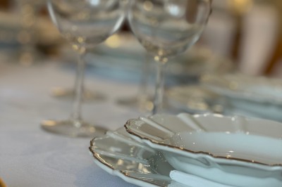 Allée centrale décorée de fleurs blanches menant à une arche florale, entourée de chaises blanches en extérieur.