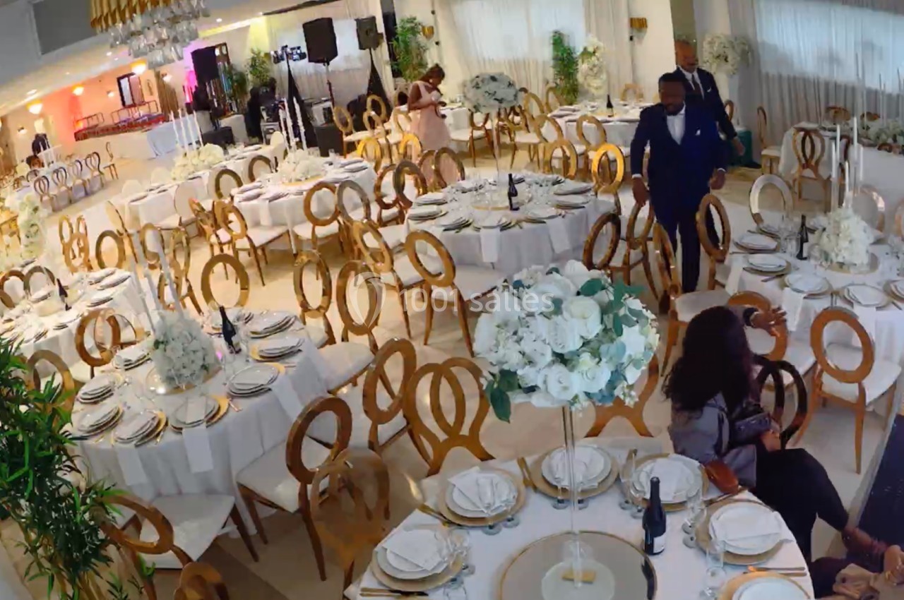 Salle de réception élégante avec tables rondes décorées de nappes blanches, vaisselle raffinée et arrangements floraux.