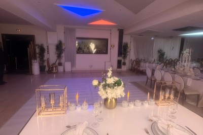 Allée centrale décorée de fleurs blanches menant à une arche florale, entourée de chaises blanches en extérieur.