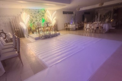 Allée centrale décorée de fleurs blanches menant à une arche florale, entourée de chaises blanches en extérieur.