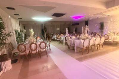 Allée centrale décorée de fleurs blanches menant à une arche florale, entourée de chaises blanches en extérieur.