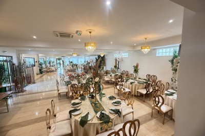 Allée centrale décorée de fleurs blanches menant à une arche florale, entourée de chaises blanches en extérieur.