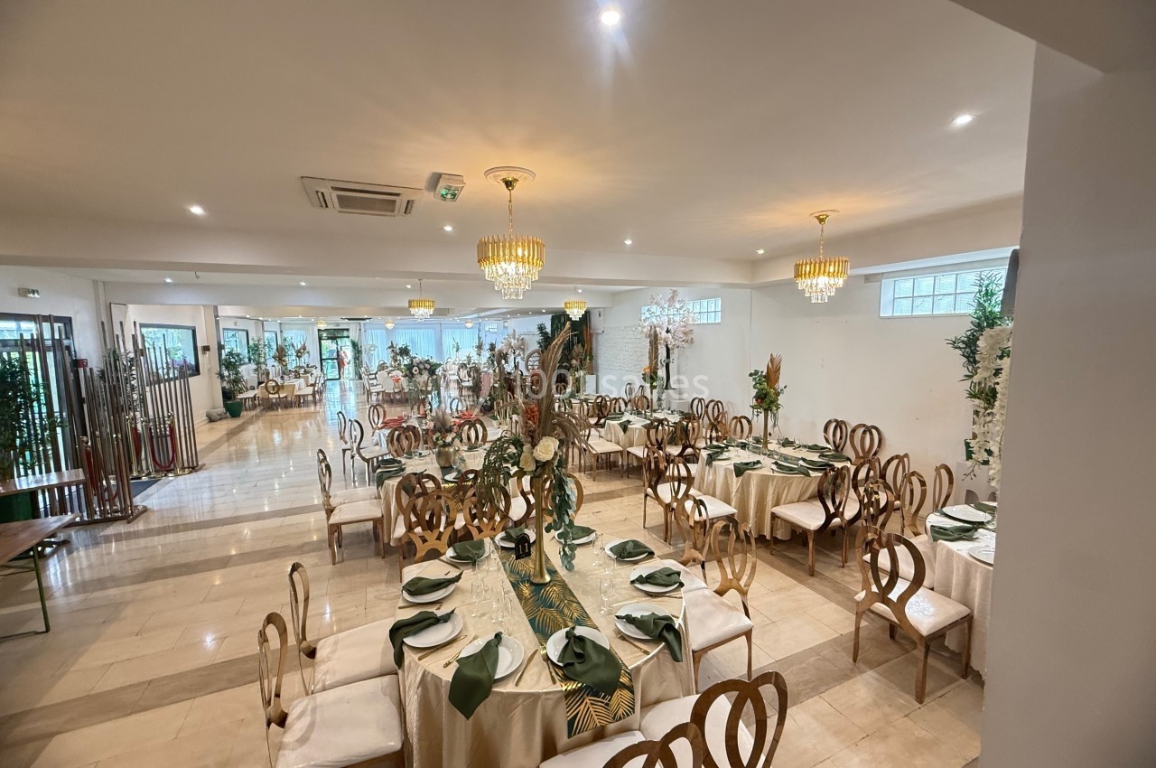 Salle de réception élégante avec tables dressées, chaises en bois, nappes beiges et décorations florales.
