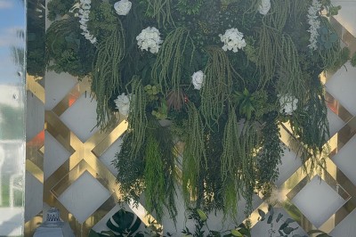 Allée centrale décorée de fleurs blanches menant à une arche florale, entourée de chaises blanches en extérieur.