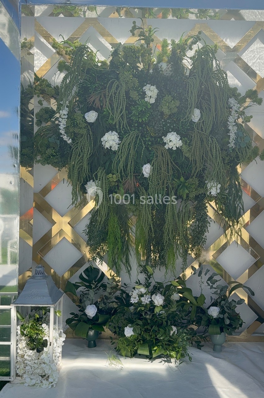 Mur végétal orné de plantes vertes et de fleurs blanches, avec une lanterne décorative posée au sol.