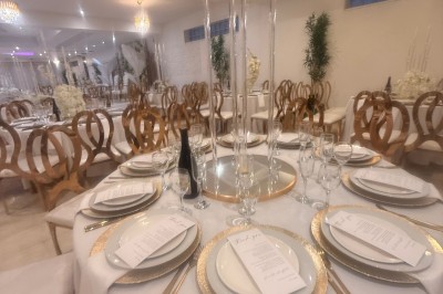 Allée centrale décorée de fleurs blanches menant à une arche florale, entourée de chaises blanches en extérieur.