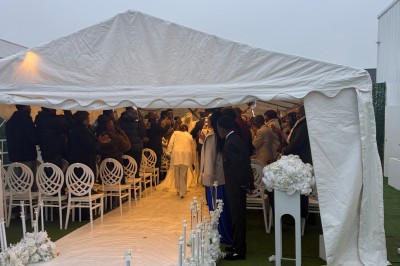 Allée centrale décorée de fleurs blanches menant à une arche florale, entourée de chaises blanches en extérieur.