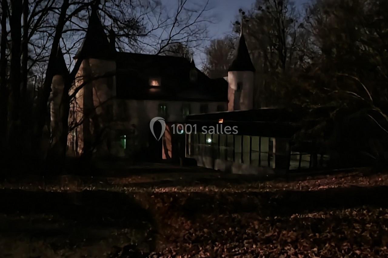 Château éclairé la nuit, entouré d'arbres et d'un sol couvert de feuilles.