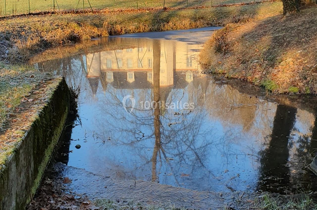 Reflet d'un château blanc entouré d'arbres dans un petit cours d'eau par une journée ensoleillée d'hiver.