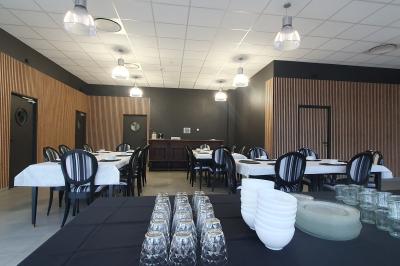 Salle de réception avec tables dressées, chaises noires, murs sombres et un buffet en arrière-plan.