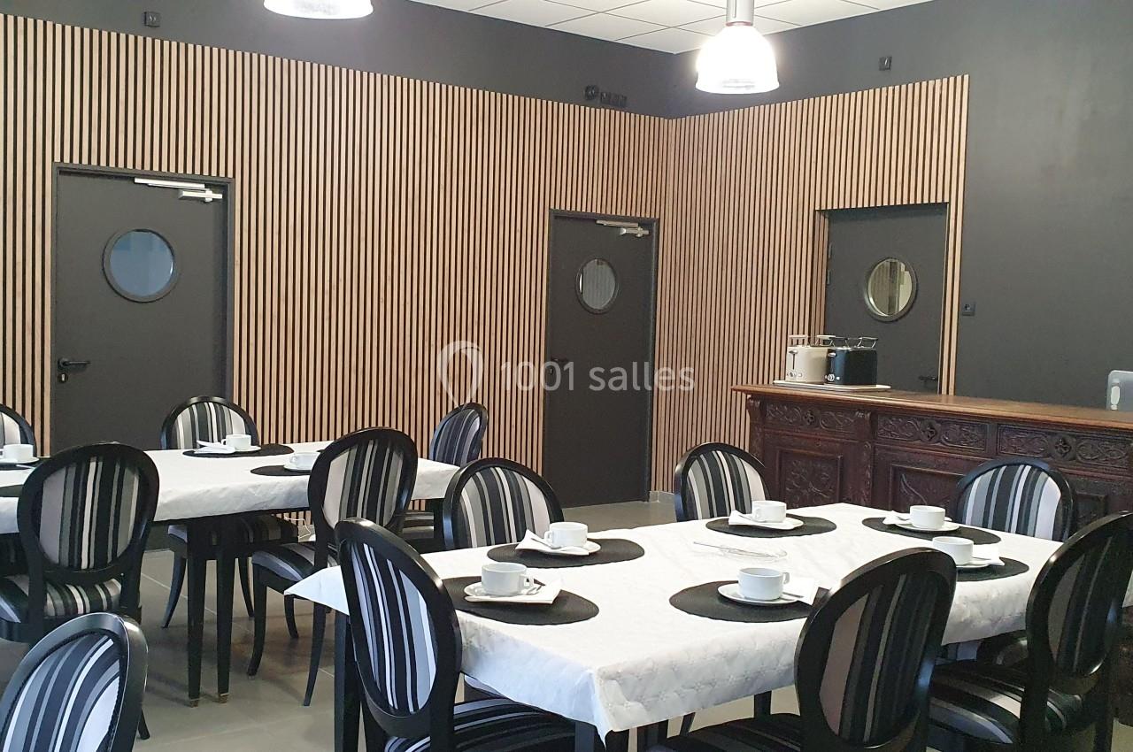 Salle à manger avec tables dressées, chaises noires, murs en bois et comptoir ancien en bois sombre.