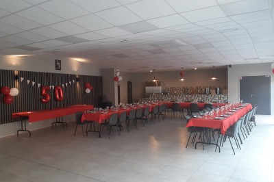 Salle décorée pour un 50e anniversaire, avec tables alignées, nappes rouges et ballons suspendus.