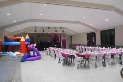 Salle décorée pour un 50e anniversaire, avec tables alignées, nappes rouges et ballons suspendus.