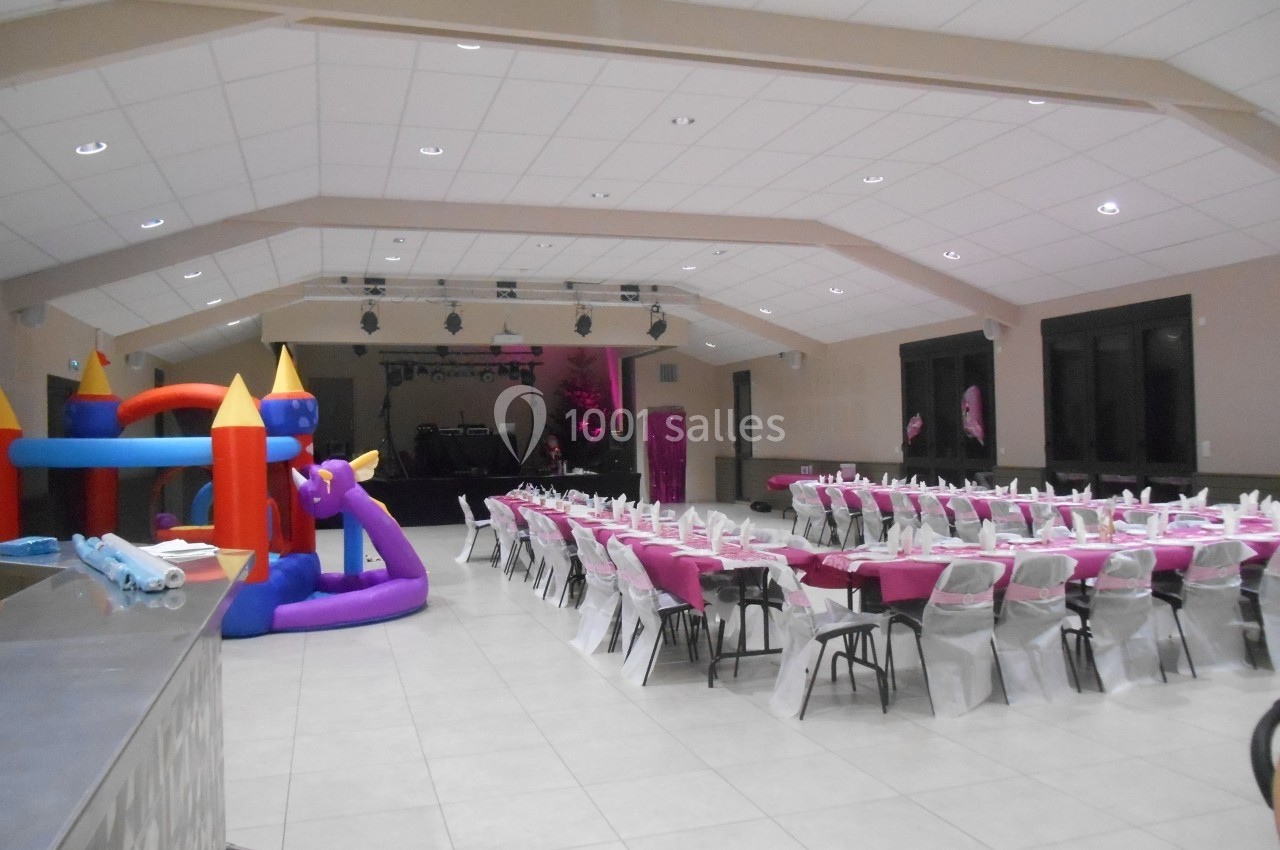 Salle de réception décorée avec des tables dressées en rose et blanc, et une structure gonflable colorée au premier plan.